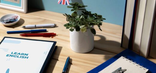 Desk with a Learn English workbook, pens, and a small plant; a UK flag backdrop and stacked books on a wooden surface.