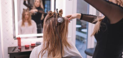 Los servicios de peluquería amplían sus propuestas para responder a nuevas necesidades - Hairstylist curling a client's hair with rollers in a bright salon, reflected in the mirror behind them.